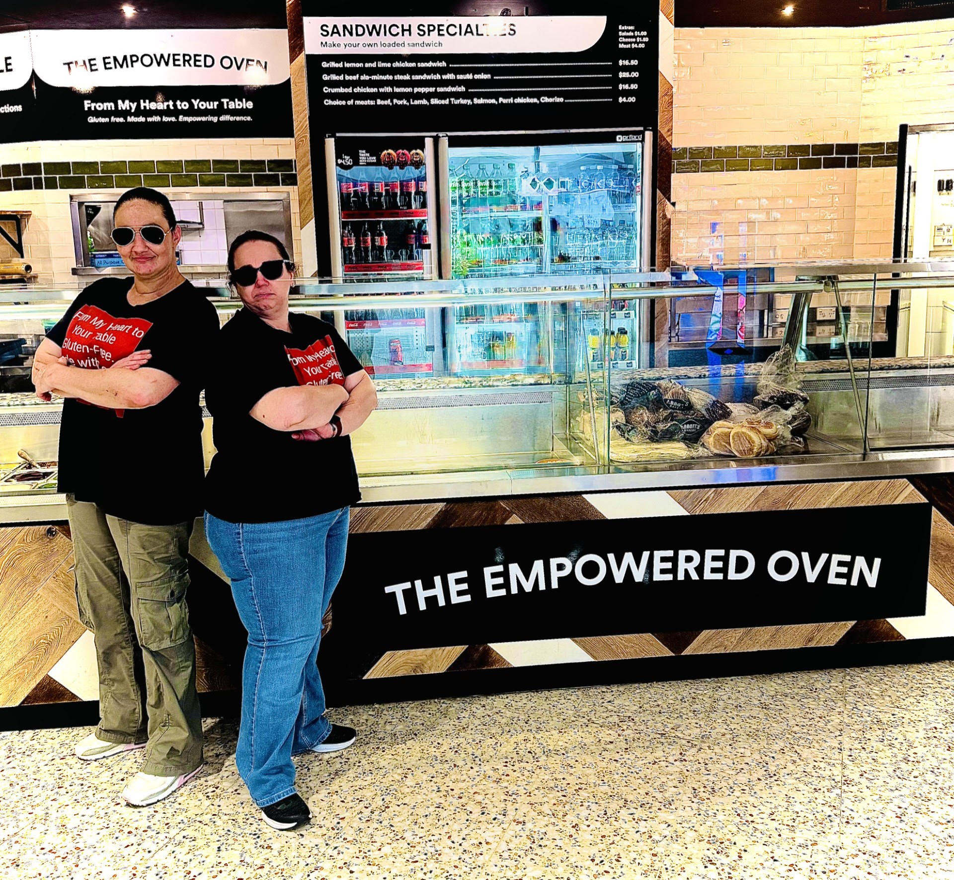 Two Empowered Oven team members standing in front of the storefront signage at their retail counter